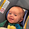 Jax is registered to the contest to win money with this photo: baby, child, car_seat, smiling, tongue_out, toy, blue, green_clothing, infant, cute, indoor, seatbelt, warning_label, head_support, happy, person, young_child, closeup, portrait, safety