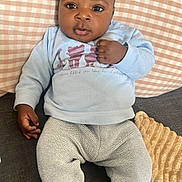 Noah a rejoint le concours — aidez-le/la à gagner de superbes lots ! baby, infant, couch, pillow, knit_pants, sweatshirt, socks, indoor, child, person, face, hand, footwear, seated, looking_at_camera, curious, soft_lighting, cozy, relaxed, home