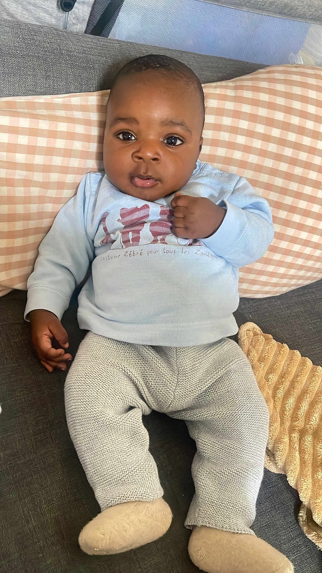 Noah a rejoint le concours — aidez-le/la à gagner de superbes lots ! baby, infant, couch, pillow, knit_pants, sweatshirt, socks, indoor, child, person, face, hand, footwear, seated, looking_at_camera, curious, soft_lighting, cozy, relaxed, home