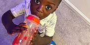 Akaiyo is registered to the contest to win money with this photo: child, toddler, sippy_cup, carpet, indoor, topknot, blue_slippers, captain_america, shorts, curious, looking_up, holding, drinking, person, floor, casual_clothing, playful, wide_eyes, young_child, home
