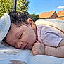baby, sleeping, blanket, outdoor, sunlight, curly_hair, peaceful, face, hand, skin, infant, soft_texture, nature, blue_sky, cloud, roof, daylight, portrait, cozy, relaxation