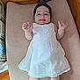 baby, child, infant, smile, white_dress, headband, polka_dot, crib, cushion, wooden_furniture, sock, happy, cute, indoor, person, baby_clothing, lying_down, toddler, face, small_hands