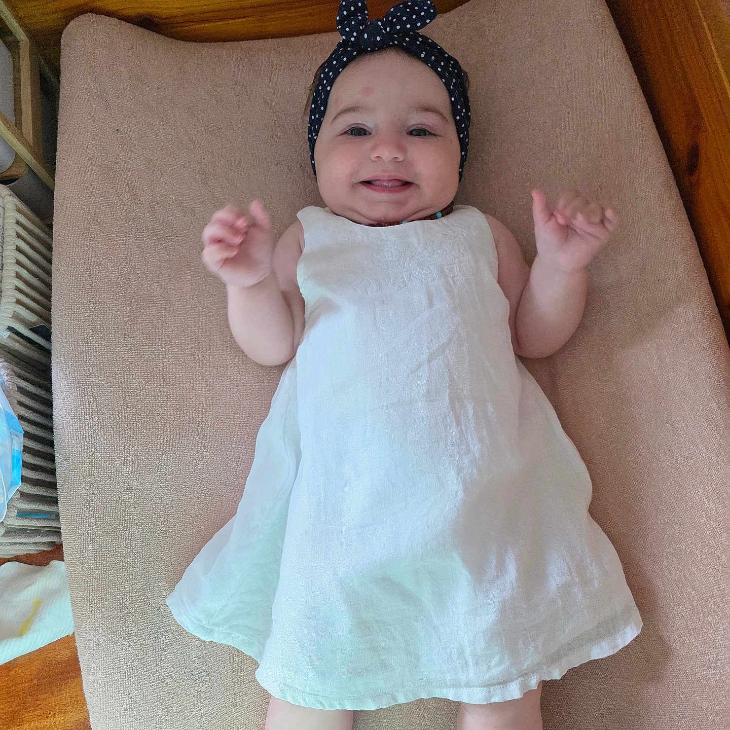 Luna a rejoint le concours — aidez-le/la à gagner de superbes lots ! baby, baby_clothing, child, crib, cushion, cute, face, happy, headband, indoor, infant, lying_down, person, polka_dot, small_hands, smile, sock, toddler, white_dress, wooden_furniture