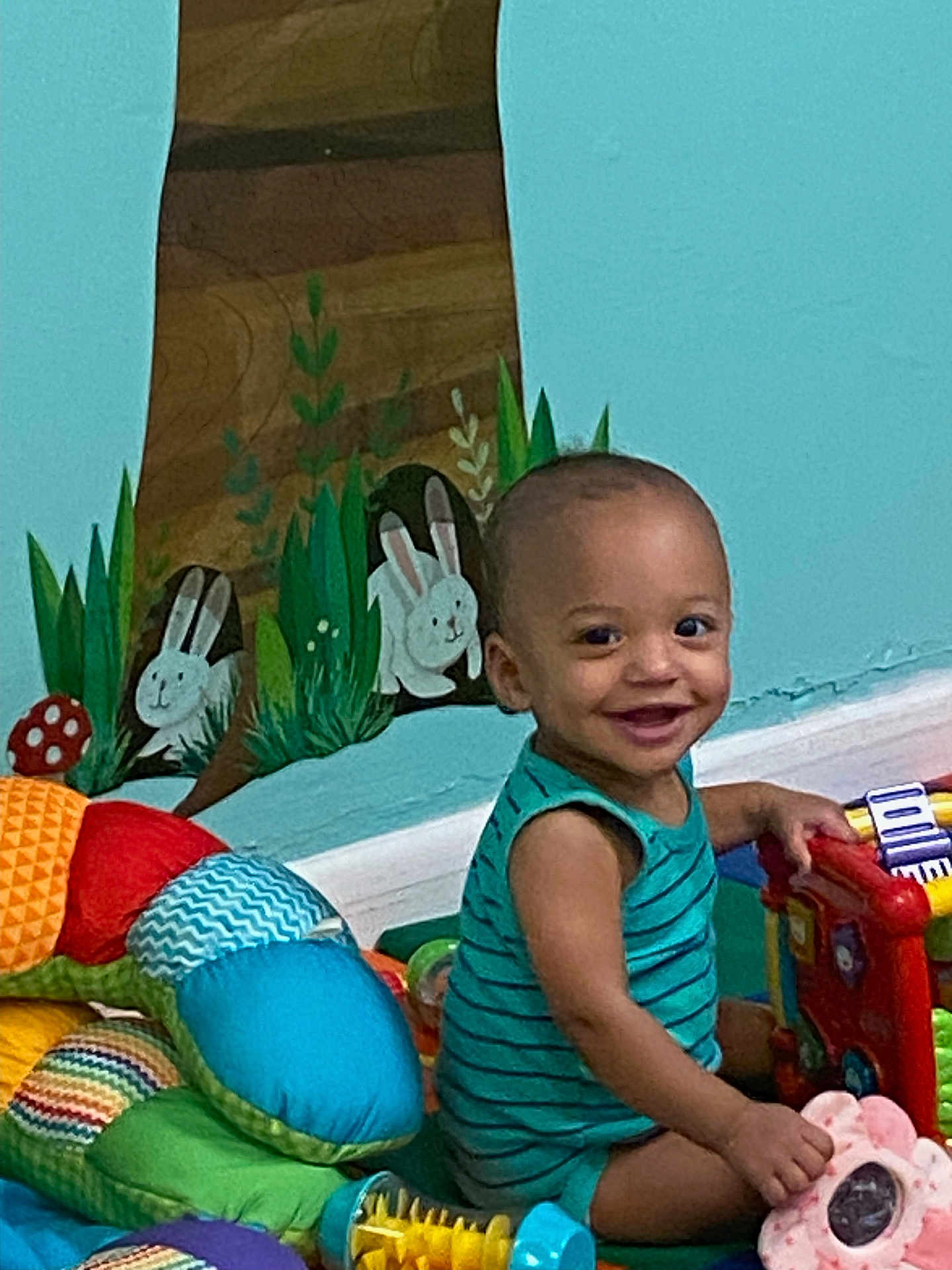 Xzavion joined the competition — help win amazing prizes! toddler, child, smiling, toy, colorful, onesie, indoor, playtime, baby, mural, wall_painting, bunny, greenery, floor, soft_toys, piano_toy, cute, happy, person, room