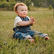 Walker joined the competition — help win amazing prizes! toddler, child, grass, outdoor, nature, field, barefoot, overalls, clapping, curly_hair, cute, sitting, daylight, greenery, happy, portrait, baby, casual_clothing, young_child, smile