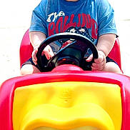 Walker is registered to the contest to win money with this photo: baby, blue_shirt, child, cute, driveway, green_sunglasses, house, outdoor, plastic_toy, playful, portrait, reflection, rolling_stones_tshirt, steering_wheel, sunglasses, sunny, toddler, tongue_out, toy_car, vehicle