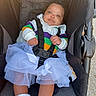 baby, booties, casual_wear, child, colorful_clothing, curly_hair, cute, fabric_texture, happy_expression, infant, outdoor, person, portrait, seat, seatbelt, sitting, soft_light, stroller, tutu, white_fabric