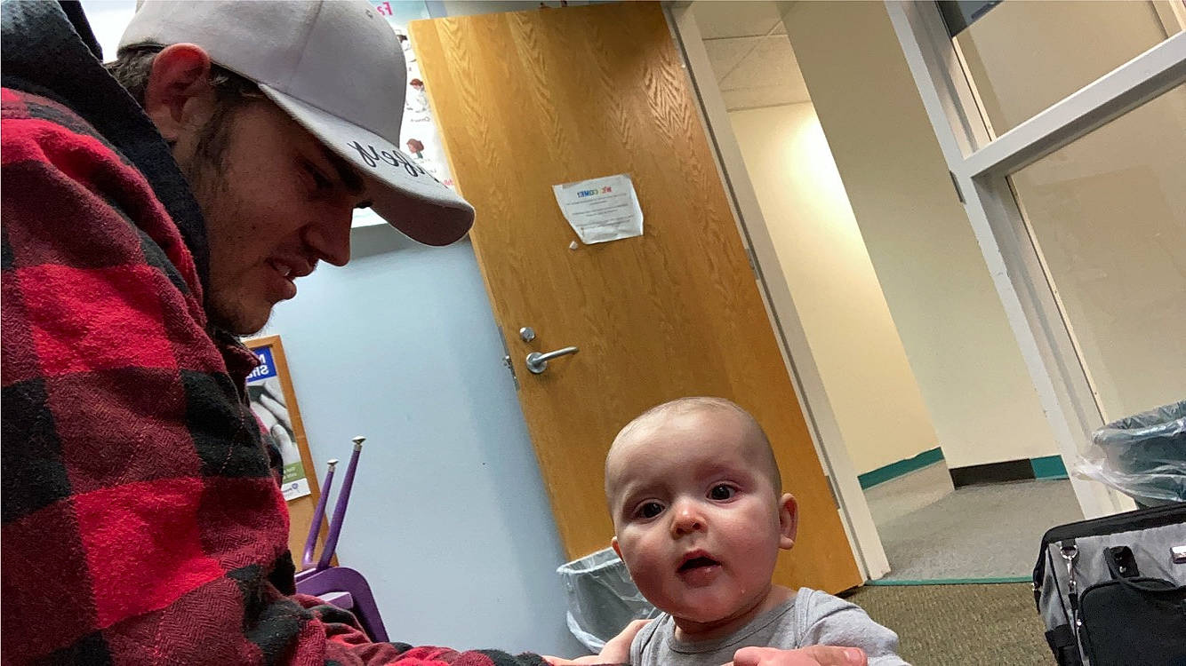 Christopher is registered to the contest to win money with this photo: baby, baseball_cap, cap, child, conversation, event, eyewear, flooring, fun, headwear, hearing, job, mouth, person, room, sitting, surprise, toddler