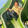 child, slide, playground, outdoor, smiling, boots, tan_jacket, green_slide, happy, fun, kid, recreation, park, activity, daylight, play, clothing, person, leisure, youth