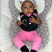 Maya joined the competition — help win amazing prizes! baby, infant, child, headband, bow, pink_pants, black_bib, cat_design, socks, patterned_seat, cushion, indoor, person, cute, portrait, seated, small_hands, looking_at_camera, clothing, soft_fabric