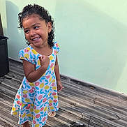 Léna participe au concours pour gagner de l'argent avec cette photo : candid, child, colorful_dress, curly_hair, dress, earring, feet, girl, happy, outdoor, patterned_dress, playful, portrait, sandals, shadow, smiling, standing, sunlight, wall, wooden_deck