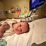 baby, infant, hospital, medical_equipment, bed, blanket, face, person, lying_down, patient, healthcare, closeup, cute, newborn, gaze, indoors, monitor, pacifier, clothing, soft_lighting