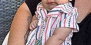 Yariel joined the competition — help win amazing prizes! baby, infant, child, person, arm, clothing, striped_shirt, blue_eyes, pacifier_clip, tattoo, outdoor, furniture, chair, wicker, adult, holding, skin, closeup, cute, relaxed