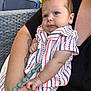 baby, infant, child, person, arm, clothing, striped_shirt, blue_eyes, pacifier_clip, tattoo, outdoor, furniture, chair, wicker, adult, holding, skin, closeup, cute, relaxed