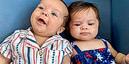 Emily is registered to the contest to win money with this photo: baby, infant, child, couch, blue_couch, striped_shirt, floral_dress, two_children, cute, portrait, indoor, smiling, curious, sitting, people, face, eyes, skin, hair, american_flag_emoji