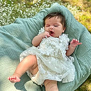 Emily is registered to the contest to win money with this photo: baby, infant, white_dress, lace, blanket, outdoor, grass, flowers, cute, child, portrait, nature, soft_texture, playful, skin, hand, foot, young, lying_down, sunlight