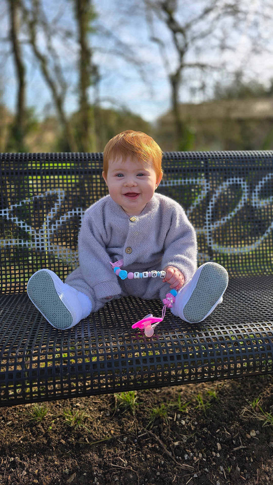 Théona participe au concours pour gagner de l'argent avec cette photo : baby, toddler, red_hair, smiling, bench, park, outdoors, grass, trees, sweater, shoes, pacifier, toy, pacifier_clip, sitting, portrait, bokeh, sunlight, cute, happy