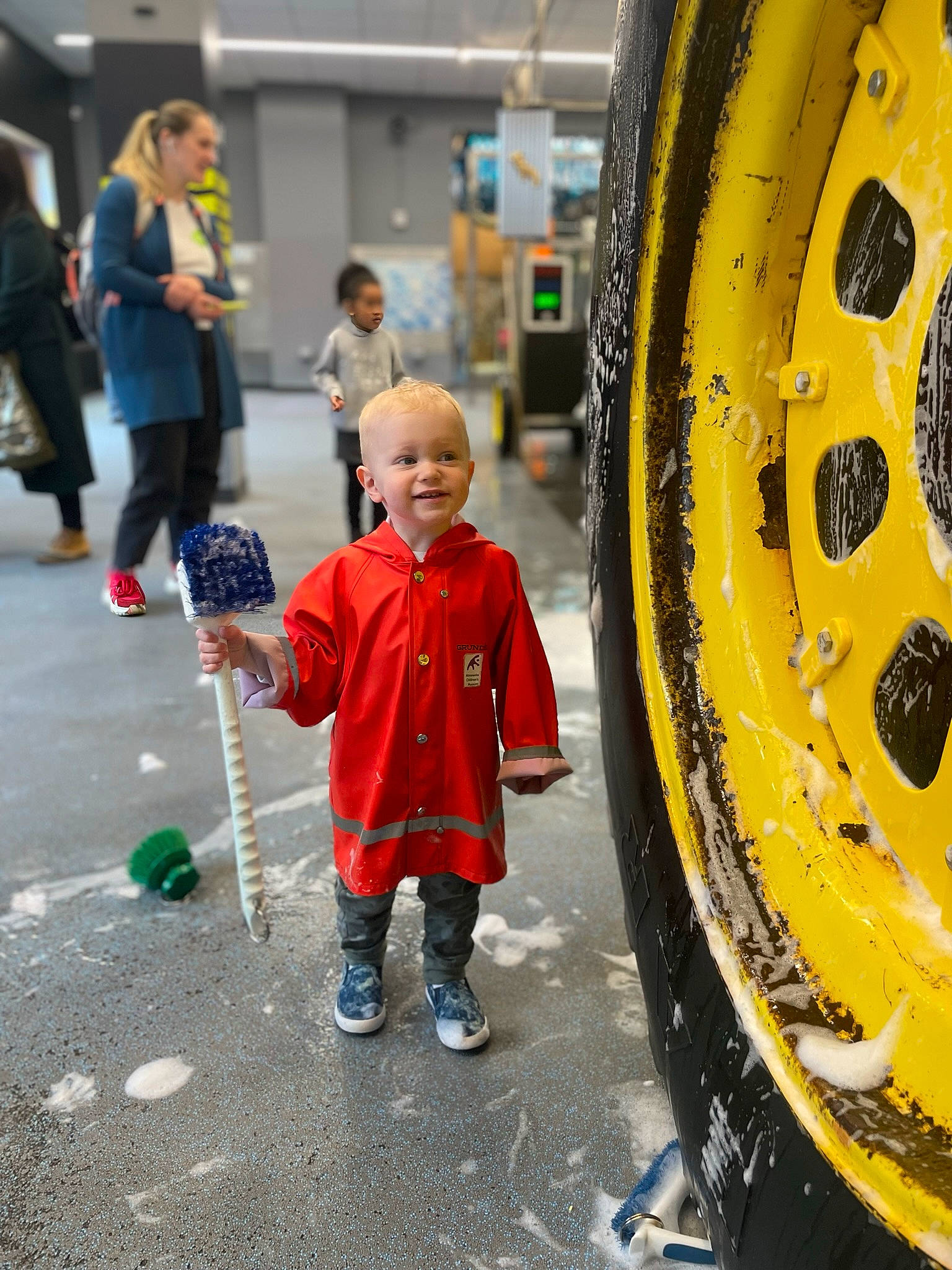 Dexter is registered to the contest to win money with this photo: asphalt, automotive_tire, blurred, fender, hubcap, jacket, joy, motor_vehicle, outerwear, person, rim, road, road_surface, rolling, sidewalk, smile, synthetic_rubber, tire, tire_care, toddler