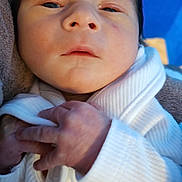 Anthony is registered to the contest to win money with this photo: baby, newborn, infant, close_up, face, hands, white_clothing, teddy_bear_patch, soft_texture, blue_background, cute, small_hands, portrait, indoors, child, baby_clothes, skin, person, newborn_baby, sleepy