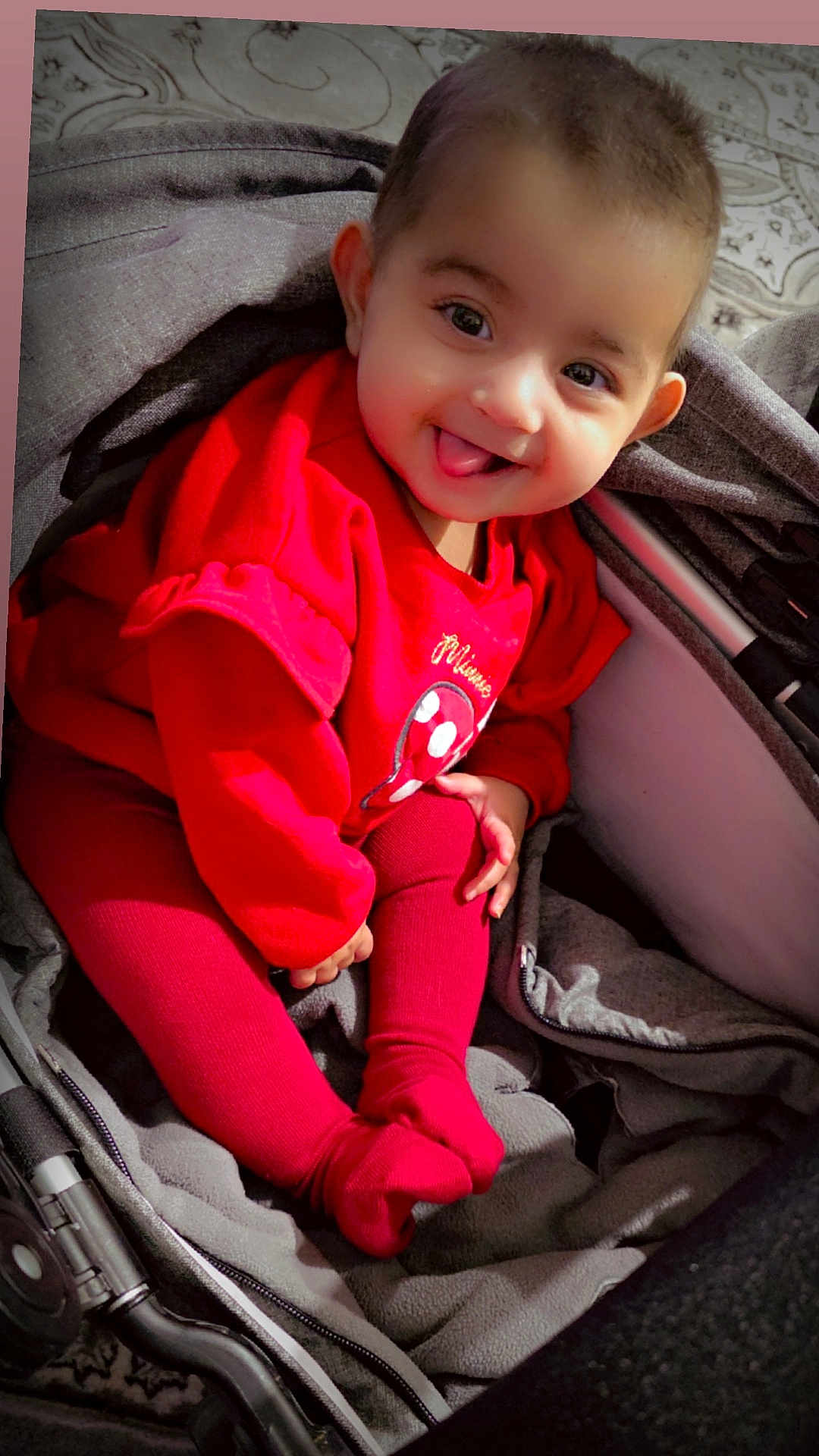 Ameera is registered to the contest to win money with this photo: baby, child, smiling, tongue_out, red_clothing, leggings, stroller, blanket, indoor, cute, happy, person, face, infant, playful, cozy, soft_lighting, portrait, sitting, young_child