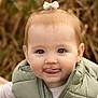 toddler, child, face, expression, tongue, bow, hair, vest, green, outdoor, nature, portrait, cute, baby, smile, warm_clothing, young_child, person, closeup, funny_face
