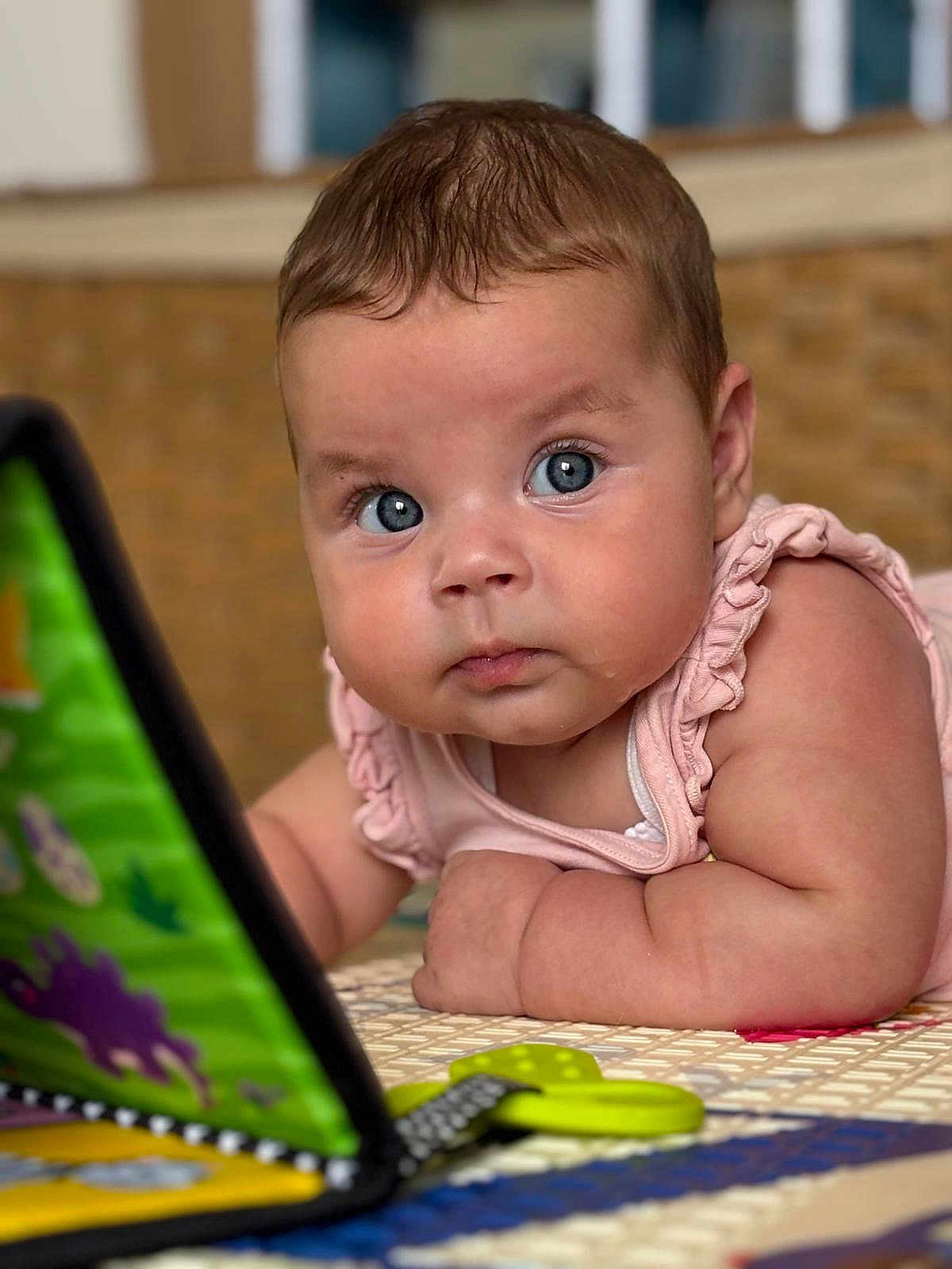 Selena participe au concours pour gagner de l'argent avec cette photo : baby, blue_eyes, curious, play_mat, toy_book, indoor, close_up, infant, child, colorful, soft_lighting, face, skin, arm, clothing, pink_outfit, expression, young_child, focus, floor
