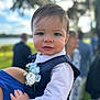 child, toddler, baby, face, person, clothing, vest, flower, boutonniere, hand, outdoor, blurred_background, nature, people, portrait, smile, short_hair, blue, white, holding