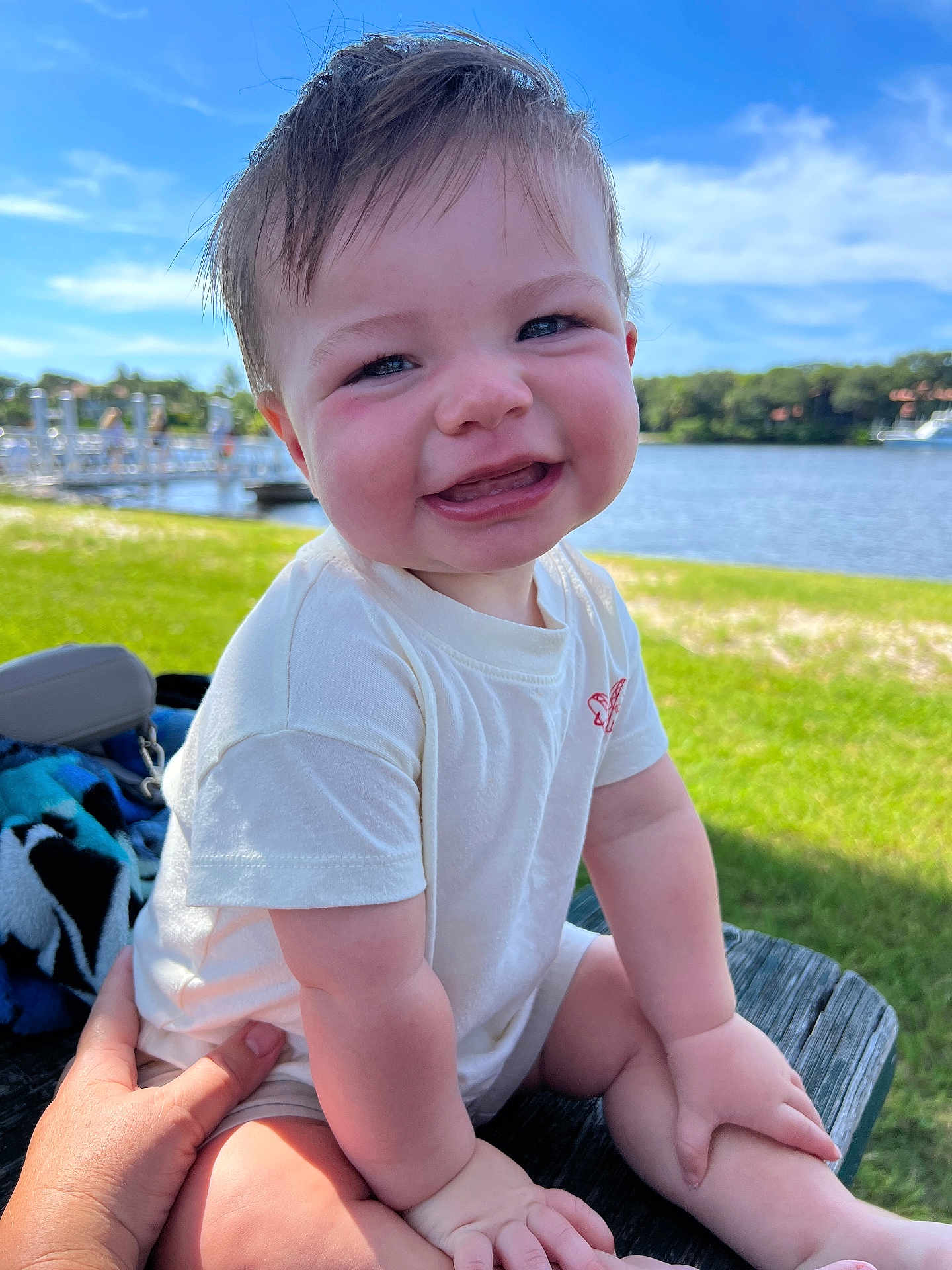 Finn joined the competition — help win amazing prizes! baby, child, smiling, outdoor, grass, water, lake, sky, clouds, person, hand, wood, bench, sunlight, tshirt, happy, portrait, nature, summer, daytime