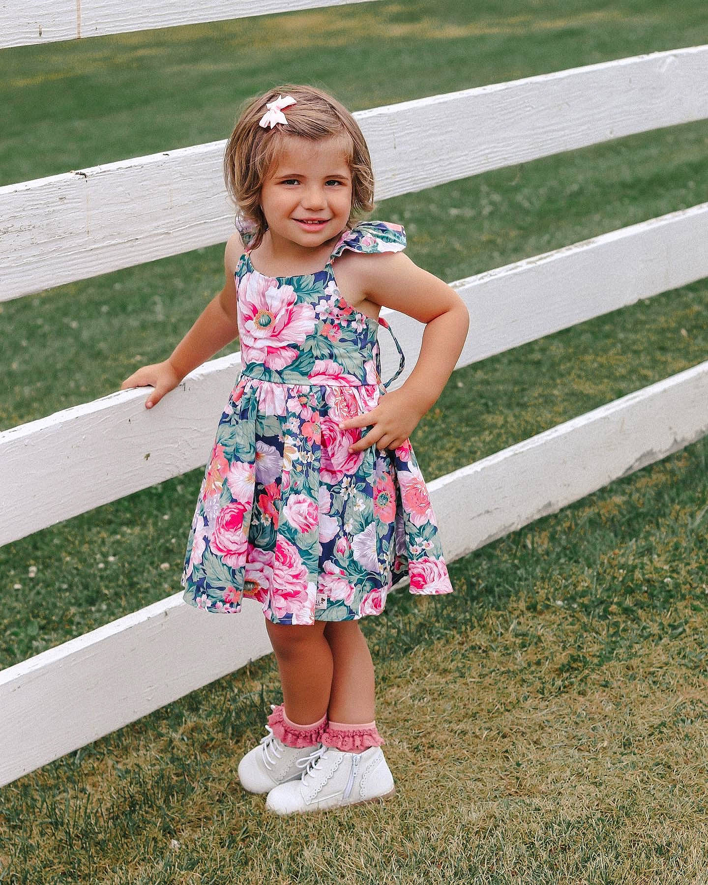 Hayden is registered to the contest to win money with this photo: baby_toddler_clothing, dress, fence, footwear, fun, grass, hair, happy, joy, leg, leisure, people_in_nature, person, pink, plant, public_space, shoe, smile, sneakers, standing