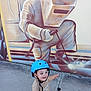 toddler, child, helmet, bike, concrete, mural, painting, welder, protective_gear, outdoor, smiling, pointing, playful, casual_clothing, blue_helmet, art, wall_art, street_art, young_child, sidewalk