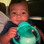 Gianni is registered to the contest to win money with this photo: baby, chair, child, closeup, clothing, cute, dark_shirt, drinking, expression, face, furniture, hand, holding, indoor, infant, milk, milk_spill, person, sippy_cup, young_child