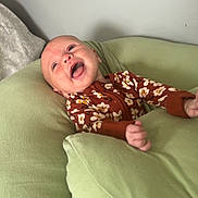 Ophelia is registered to the contest to win money with this photo: baby, infant, smiling, happy, cushion, green, onesie, floral_pattern, indoor, relaxing, child, person, cute, soft_furniture, head, small_hand, lying_down, cheerful, skin, portrait