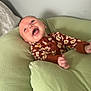 baby, infant, smiling, happy, cushion, green, onesie, floral_pattern, indoor, relaxing, child, person, cute, soft_furniture, head, small_hand, lying_down, cheerful, skin, portrait