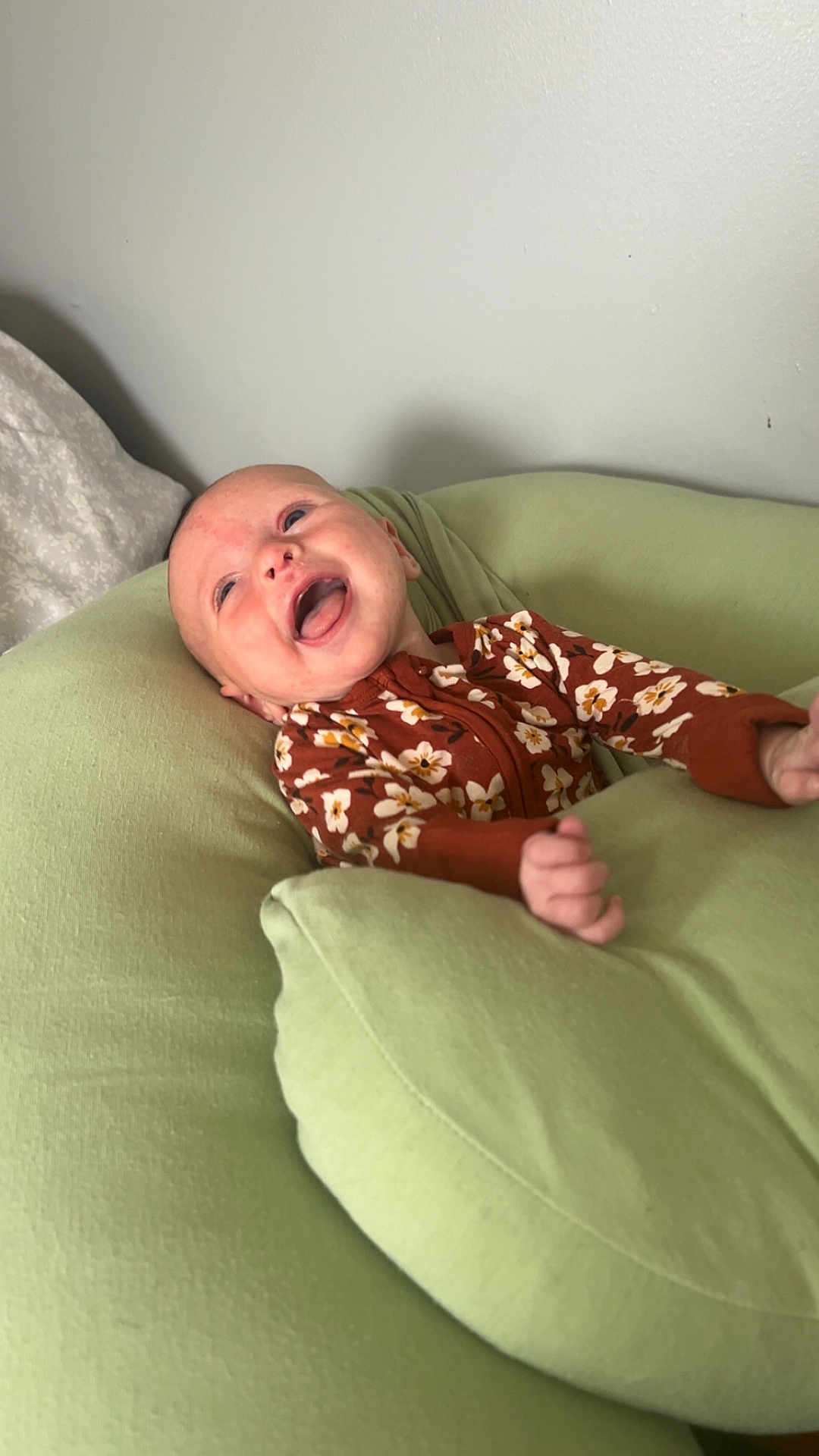Ophelia is registered to the contest to win money with this photo: baby, infant, smiling, happy, cushion, green, onesie, floral_pattern, indoor, relaxing, child, person, cute, soft_furniture, head, small_hand, lying_down, cheerful, skin, portrait
