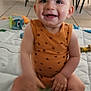 arm, baby, child, clothing, face, floor, foot, furniture, happy, head, indoor, leg, orange, pacifier, playmat, polka_dot, sitting, smiling, tile_floor, toy