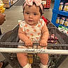 baby, child, shopping_cart, grocery_store, headband, pink_bow, dress, peach_pattern, white_shoes, socks, person, aisle, products, supermarket, shopping, floor, hand, grip, cute, portrait