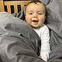 Arthur is registered to the contest to win money with this photo: baby, blanket, child, comfort, cozy, cute, expression, face, happy, indoor, infant, portrait, seated, smiling, soft_lighting, warm, white_clothing, wooden_chair, wrapped, young_child