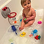 baby, bathtub, bubbles, toy, rubber_duck, elephant_basketball_hoop, child, bath_time, water, foam, blue_fish_toy, red_sunglasses, green_ball, plastic_toys, cute, indoors, skin, playful, fun, sitting