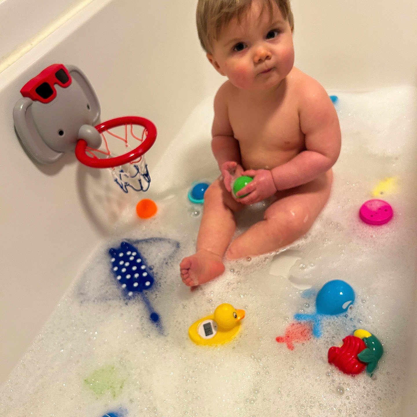 Arthur is registered to the contest to win money with this photo: baby, bath_time, bathtub, blue_fish_toy, bubbles, child, cute, elephant_basketball_hoop, foam, fun, green_ball, indoors, plastic_toys, playful, red_sunglasses, rubber_duck, sitting, skin, toy, water