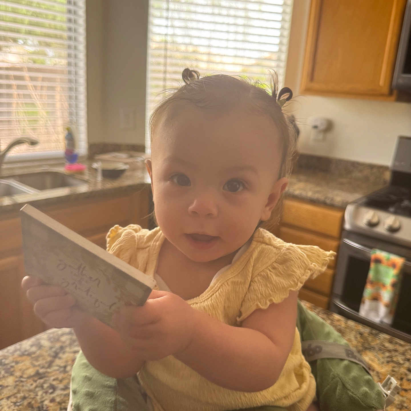 Yasenia joined the competition — help win amazing prizes! toddler, child, baby, indoor, kitchen, countertop, window, blinds, book, seat, cushion, yellow_clothing, hair_ties, curious, person, face, light, cabinet, stove, appliance