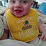 Addison joined the competition — help win amazing prizes! baby, bib, smile, blanket, indoor, child, happy, face, clothing, infant, person, cute, young, cozy, home, portrait, hand, sitting, text_on_bib, yellow_bib