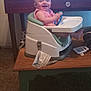baby, child, booster_seat, table, toy, indoor, carpet, furniture, smiling, happy, person, seat, wood, desk, foot, clothing, play, infant, face, holding