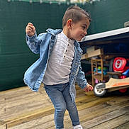 Adriano participe au concours pour gagner de l'argent avec cette photo : boy, casual_clothing, child, daylight, denim_jacket, fence, happy, jeans, motion, outdoor, person, playful, portrait, short_hair, smiling, toy_vehicle, white_shirt, white_shoes, wooden_deck, young