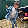 boy, casual_clothing, child, daylight, denim_jacket, fence, happy, jeans, motion, outdoor, person, playful, portrait, short_hair, smiling, toy_vehicle, white_shirt, white_shoes, wooden_deck, young