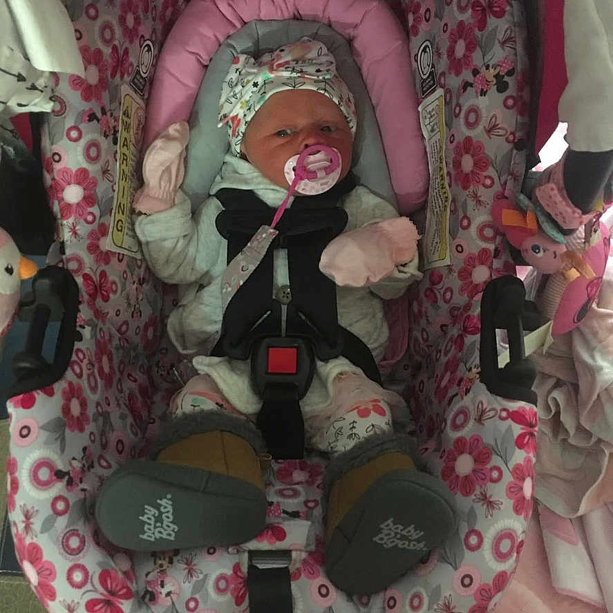 Chloe is registered to the contest to win money with this photo: baby, car_seat, pacifier, mittens, hat, blanket, toy, infant, child, clothing, pink, floral_pattern, seatbelt, indoor, person, cute, sleepwear, soft_toys, comfort, newborn