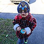 child, toddler, sunglasses, novelty_sunglasses, cat_ears, hoodie, plaid_coat, red_coat, toy, sidewalk, grass, sneakers, shoes, car, reflection, photographer, portrait, outdoor, cold_weather, cute