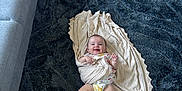 Mila is registered to the contest to win money with this photo: baby, blanket, child, comfort, couch, cozy, cute, diaper, floor, furniture, happy, home, indoors, infant, living_room, person, plush, rug, smiling, wooden_floor