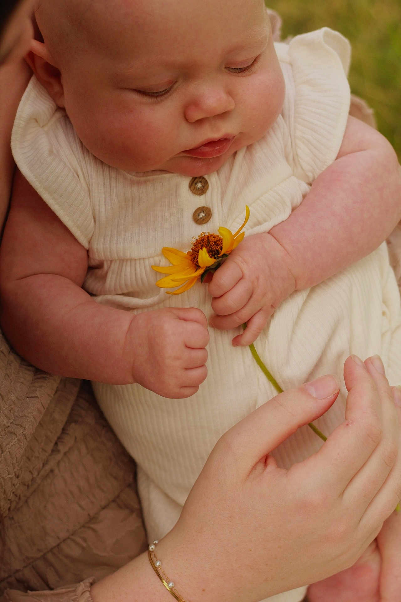Brynley is registered to the contest to win money with this photo: baby, infant, flower, hand, close_up, skin, cute, child, nature, outdoor, soft_lighting, human, portrait, holding, yellow_flower, bracelet, clothing, arm, gentle, tender