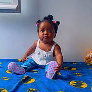 Aliah Saran participe au concours pour gagner de l'argent avec cette photo : baby, child, sitting, bed, batman_logo, blue_bedspread, pigtails, curious_expression, indoors, white_top, blue_pants, pink_booties, bracelet, necklace, window, wall, floor, cute, portrait, young_child