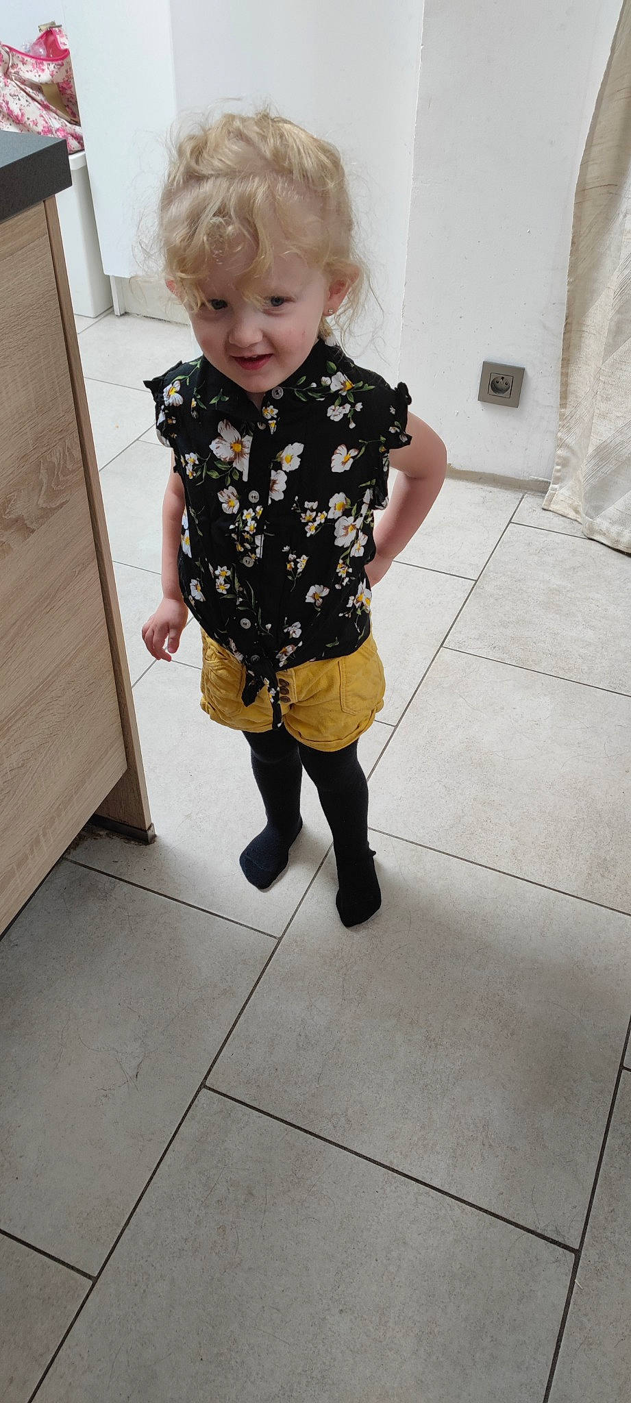 Siloé participe au concours pour gagner de l'argent avec cette photo : arm, baby_toddler_clothing, blond, child, dress, floor, flooring, hair, human_body, human_leg, joint, knee, pattern, person, shoulder, sleeve, smile, thigh, toddler, waist